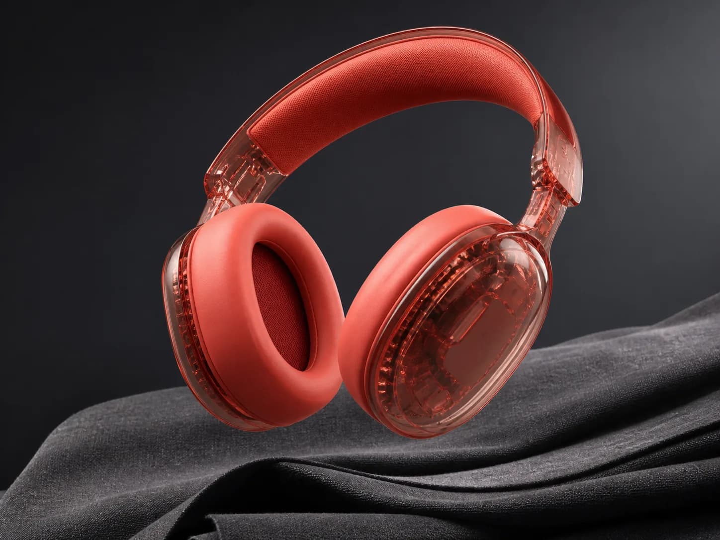 Headphone merah koral transparan melayang di atas kain abu-abu gelap