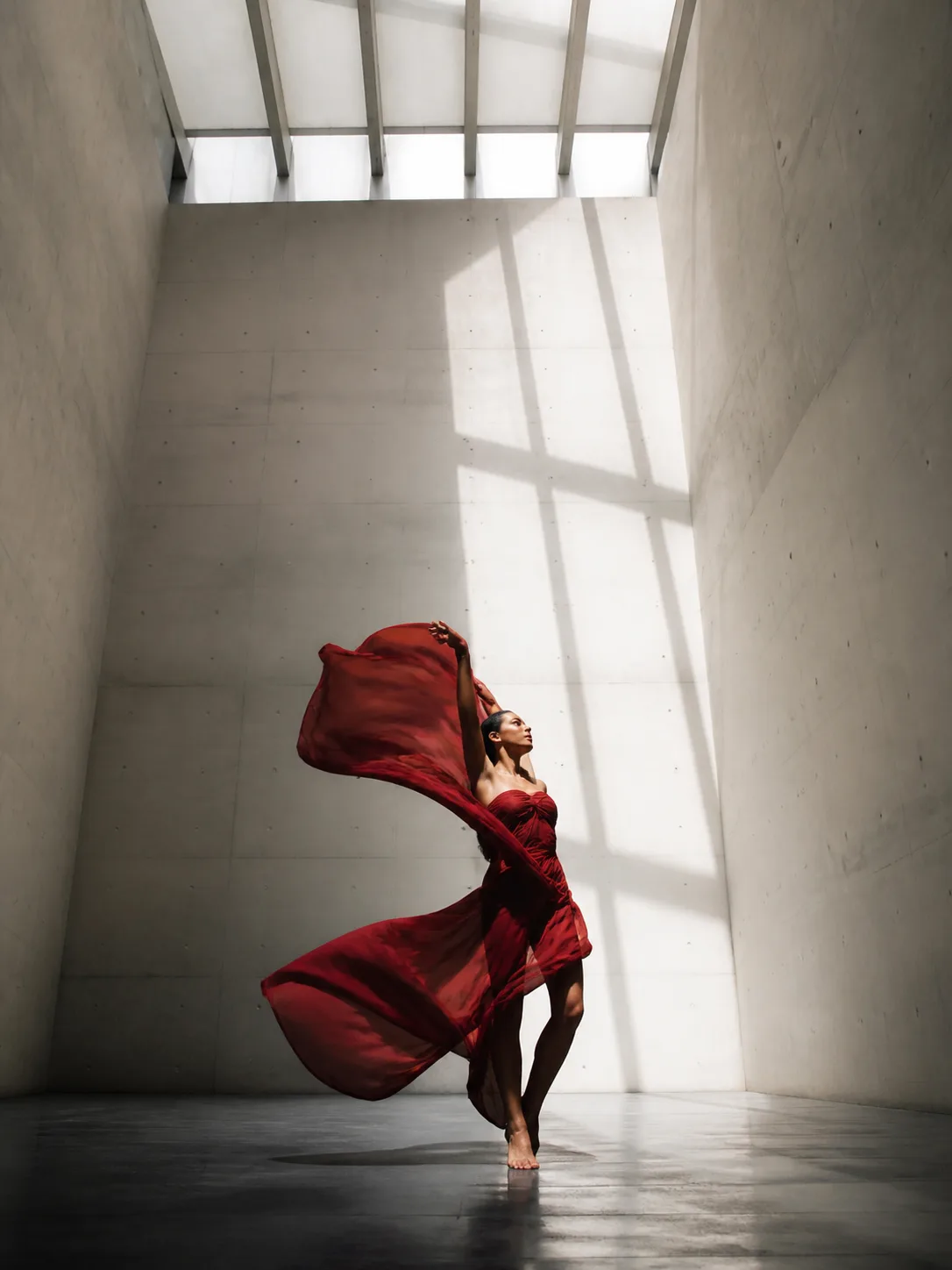 Dancer in crimson fabric inside a concrete gallery