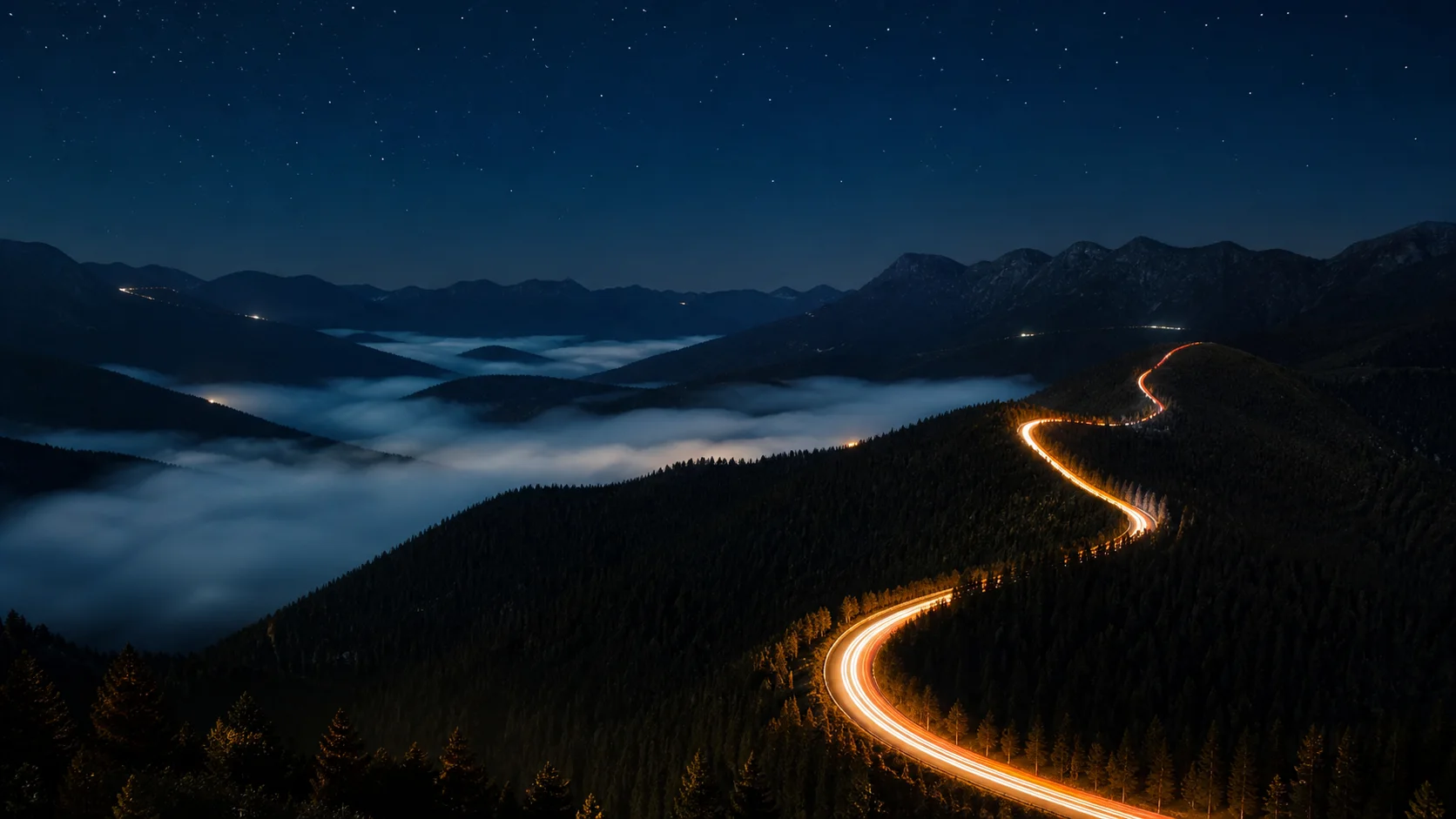 Warm highway light trails winding through dark mountains